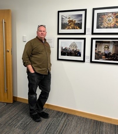 Photo of Glen Stubbe next to his photography exhibit