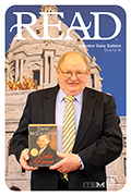 Senator Dahms is pictured in front of a backdrop of the Minnesota State Capitol while holding the book John Adams by author David McCullough.  The word READ is spelled out in all capital letters at the top of the image.